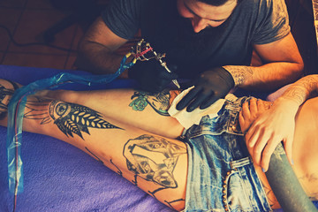 The bearded tattoo artist makes a tattoo on a woman's leg in an ink saloon.