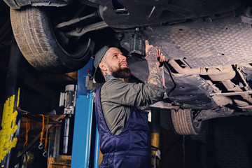 Bearded  mechanic working with the car's chassis in a workshop.