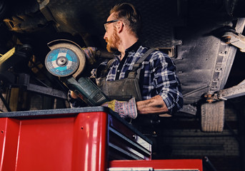 Mechanic in protective googles holds angle grinder.