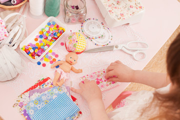 Girl sews dress dolls from pieces of fabric