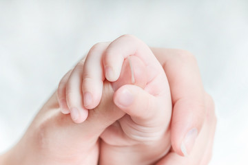 Hand of a baby holds a woman's finger
