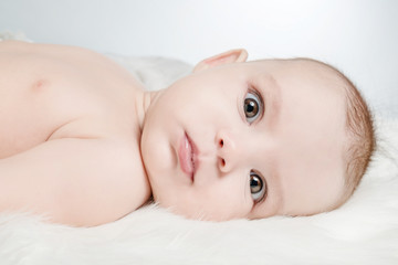 Cute baby lies on a white fluffy background and looking forward