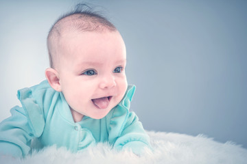 Cute baby in blue jacket shows tongue on a white fur. Toned