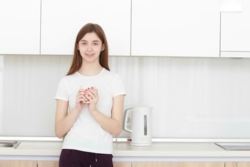 Fototapeta na wymiar Pretty young woman In a white T shirt standing in kitchen and smiling.