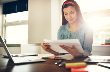 Young female entrepreneur doing paperwork at laptop