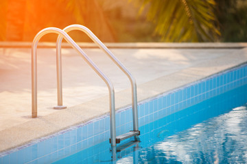 Grab bars ladder in the blue swimming pool with Orange sun light in mornung