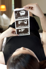 A pregnant woman wearing a black dress is holding a sonogram