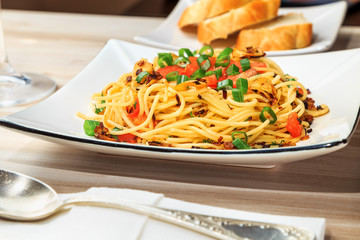 spaghetti with tomatoes, roasted garlic and green onions on a beautiful rectangular plate are on the table