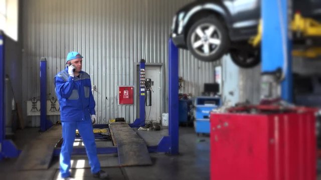 angry mechanic talking with customer near lifted car in auto repair shop.