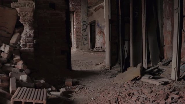 FPV CLOSE UP: Exploring decaying abandoned hotel, walking across the dark scary crumbling rooms and narrow staircase corridors. Residential brick-built building in debris. Demolished house in America