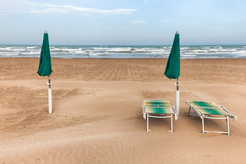 Beach chairs and two green umbrellas on sand beach in Vieste, Gargano Puglia, Italy