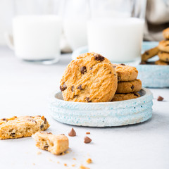 Stack of chocolate chip cookies on blue stone plate with glass of milk on light gray background. Selective focus. Copy space.