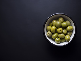Marinated whole green olives in white metal bowl with black edge isolated on black background