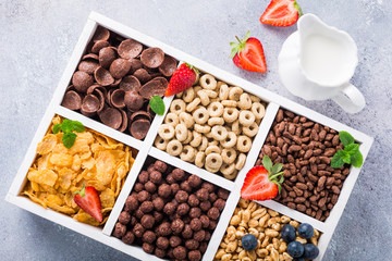 Milk jug and variety of cold quick breakfast cereals with berries in white wooden box, healthy eating concept, top view.