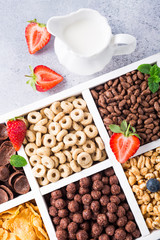 Milk jug and variety of cold quick breakfast cereals with berries in white wooden box, healthy eating concept, top view.