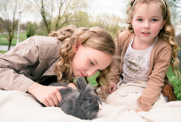 Fototapeta na wymiar two girls playing with rabbit in the park