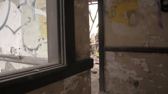 CLOSE UP FPV: Walking along a scary narrow hallway with chaotic graffiti and paint peeling from the broken walls. Destroyed attic rooms and collapsed roof in forsaken orphanage. Decay in haunted house