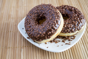 Chocolate donuts in the white plate on the light brown wooden background
