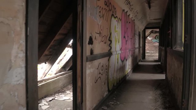 CLOSE UP FPV: Exploring a scary narrow corridor with graffiti & paint peeling from the broken walls. Destroyed attic rooms and collapsed roof in God's forsaken orphanage. Decay in ruined haunted house