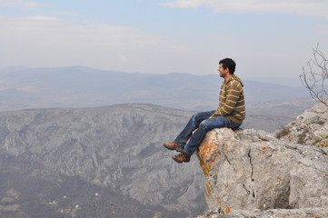 Young man sits on a cliff edge on the top of mountain with gorgeous view. Enjoying the view on the...
