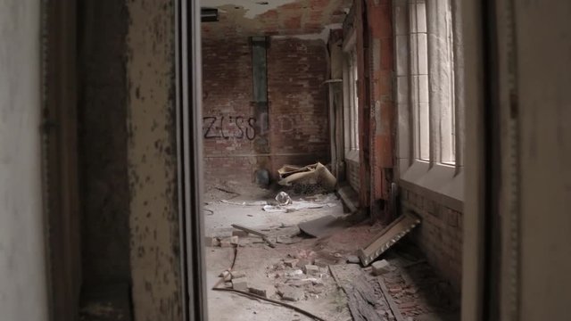 FPV CLOSE UP: Exploring decaying rooms in abandoned crumbling building. Walking through dark narrow corridor into creepy hall with broken windows and collapsing ceilings. Ruined industrial warehouse