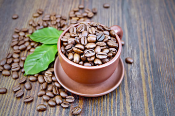 Coffee black grain in cup with leaf on board