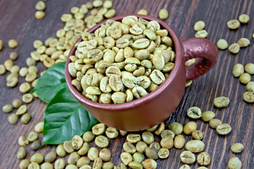 Coffee green grain in cup with leaf on board