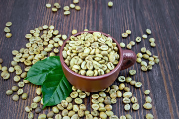 Coffee green grain in cup with leaf on dark board