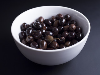 French black and brown niçoise olives in white bowl isolated on black background