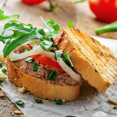 Sandwich made of grilled toasts, tuna salad, tomato, onion and arugula on a table. Delicious healthy meal for lunch.