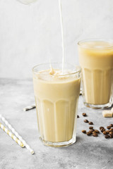 Milk pouring in ice coffee in a tall glass on a gray background