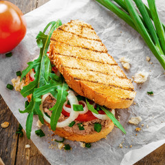 Fish sandwich made of grilled toast, tuna salad and vegetables on a rustic wooden table. Delicious healthy diet meal. Top view.