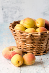  Ripe juicy apricots and peaches in a brown wicker basket on a wooden background.