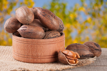 pecan nuts in a wooden bowl on the old board with blurred garden background