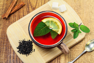 Cup of black tea with fresh mint leaves and lemon. Delicious hot healthy drink made of black tea herbals and fruits on a wooden table. Top view.