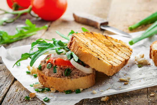 Classic tuna salad sandwich with tomato, onion and arugula on a table. Delicious healthy meal made of fish, vegetables and toasts.