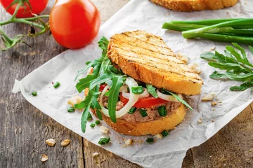 Gordijnen Delicious sandwich made of toasts, tuna, tomato, onion and arugula with ingredients on a table. Traditional healthy food. © Maxim Khytra