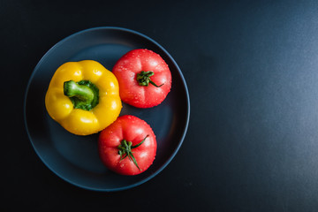 Food background - raw organic vegetables, fresh ingredients for healthily cooking on black background - bell pepper, tomatoes. Top view. Vegetarian or healthy food
