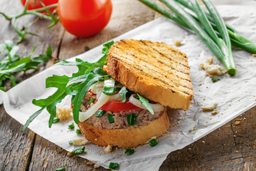 Grilled sandwich with tuna salad, tomato, onion and arugula on a wooden table. Diet healthy finger food made of toasts, vegetables and fish.