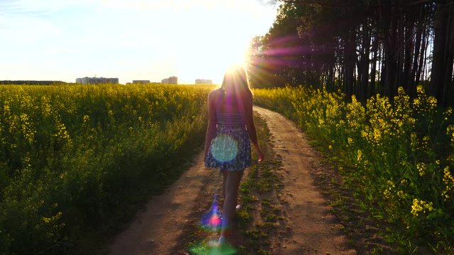 Happy girl walking and spinning on the road in the light of the setting sun.