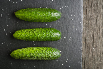 A few fresh green cucumbers lying side by side on a black stone background. A minimalistic photograph.