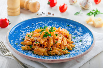 Tasty Italian penne pasta with tomato sauce on a blue rustic plate. Delicious healthy Italian food on a white wooden table.