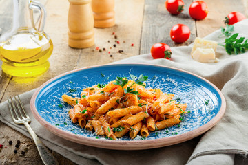 Delicious Italian penne pasta with tomato sauce and parsley on a blue plate. Traditional healthy Italian cuisine meal on a rustic wooden table.