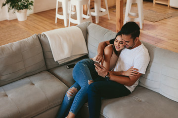 Loving couple relaxing on sofa with mobile phone