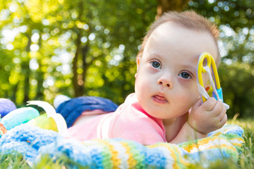 Portrait of Cute baby boy with Down syndrome lying on blanket in summer day on nature