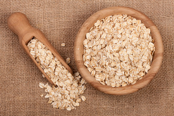Oat flakes in a wooden bowl with a scoop on sackcloth