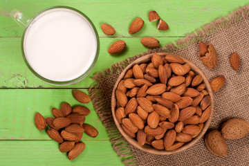 Fototapeta na wymiar Almond milk in a glass and almonds in a bowl on green wooden background. Top view
