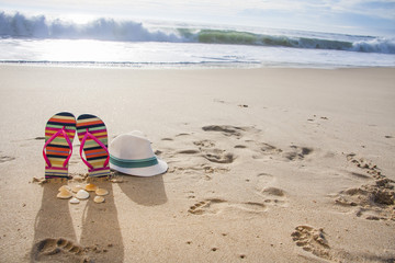 Colorful flip flops, hat and shells on the sandy beach. Vacation concept
