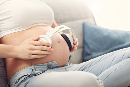 Young pregnant woman listening to music and sitting on sofa
