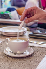 A Hand adding sugar to a cup of black coffee